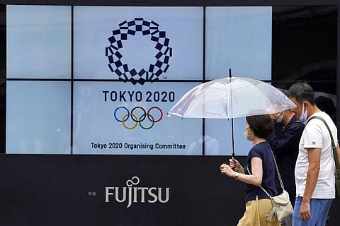People wearing face masks walk past the logo of the Tokyo 2020 Olympic Games near the Shimbashi train station. (Photo | AP)