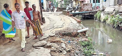 Pedestrians walk alongside a damaged road next to a drain in Cuttack. (Photo | Express)