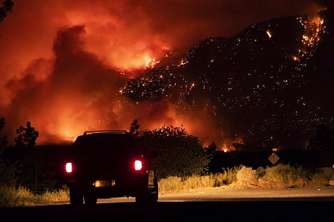 A motorist watches from a pullout on the Trans-Canada Highway as a wildfire burns on the side of a mountain in Lytton, B.C., Thursday, July 1, 2021. (Photo | AP)