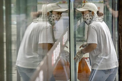 A delivery courier wearing a face mask to protect against COVID-19 is reflected in a window glass as she walks into a restaurant in Beijing. (Photo | AP)