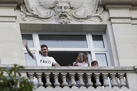 Argentinian soccer star Lionel Messi waves to supporters from his hotel balcony while his wife Antonella Roccuzzo takes photographs in Paris. (Photo | AP)