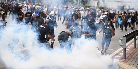 An anti-government protester tries to control smoke from a tear gas canister fired by riot police during a protest in Bangkok, Thailand. (Photo | AP)