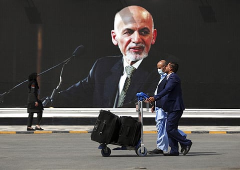 Passengers walk to the departures terminal of Hamid Karzai International Airport in Kabul, Afghanistan, on Saturday, Aug. 14, 2021, past a mural of former President Ashraf Ghani. (Photo | AP)