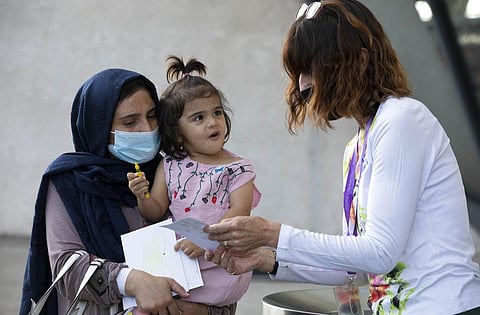 A volunteer interacts with a child evacuated from Kabul, Afghanistan at Washington Dulles International Airport. (Photo | AP)