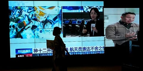 A woman walks by a TV screen showing CCTV broadcasting a news of Chinese astronauts sit inside the Shenzhou-12 manned spacecraft preparing to return to earth, Sept 16, 2021. (Photo | AP)