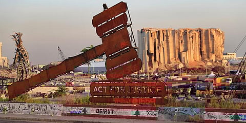 A monument that represents justice stands in front of towering grain silos that were gutted in the massive August 2020 explosion at Beirut port. (Photo | AP)