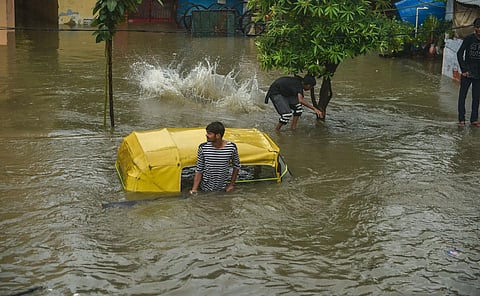 A man stands near a partially submerged auto rickshaw due to waterlogging following heavy rains in Lucknow. (Photo | PTI)
