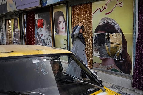A woman walks past beauty salons with window decorations which have been defaced in Kabul, Afghanistan. (Photo | AP)