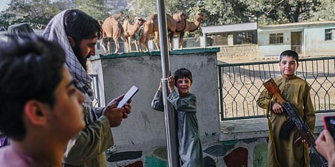 A boy poses for a picture with the rifle of a Taliban fighter near the camel enclosure in the Kabul Zoo, Sept 17, 2021. (Photo | AFP)