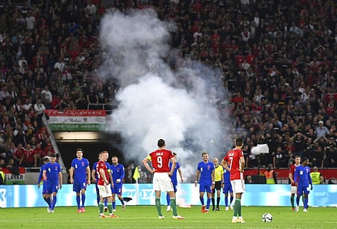 Players wait after a flare was thrown on field after England scored, during World Cup 2022 qualifier against Hungary at Puskas Ferenc Arena, Budapest, Thursday. (Photo | AP)