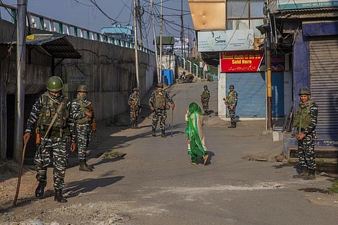 A Kashmiri woman covers her face with a scarf as she walks past paramilitary soldiers standing guard in a closed market area in Srinagar. (Photo | AP)