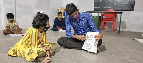 A teacher from En Maanavargal helping a child learn from a school textbook in Virudhunagar. (Photo| EPS)