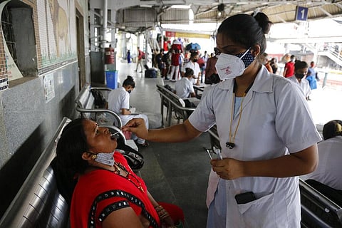 A health worker takes a swab sample of a passenger entering the city to test for COVID-19, at a railway station in Ahmedabad (Photo | AP)