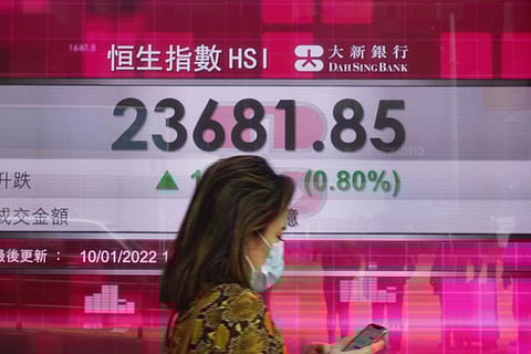 A woman walks past a bank's electronic board showing the Hong Kong share index at Hong Kong Stock Exchange. (Photo | AP)