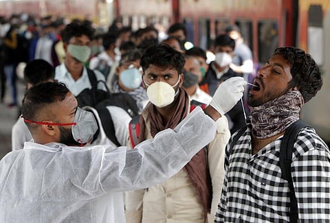A health worker collects a swab sample from a traveler at a train station to test for COVID-19 before allowing him to enter the city, in Mumbai. (Photo | AP)