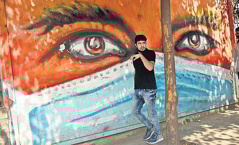 A youth without a face mask walks past an art stressing the importance of wearing one, near Town Hall in Bengaluru. (File Photo | Nagaraja Gadekal, EPS)