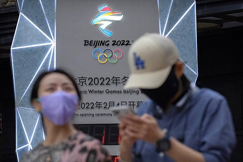 People wearing face masks to protect against COVID-19 walk past a display showing a countdown clock to the Beijing 2022 Winter Olympics in Beijing (File Photo | AP)