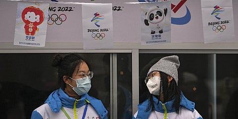 Volunteers wearing face masks to help protect from the coronavirus chat with each other at an information booth for the Beijing Winter Olympics Games at Qianmen Street.(Photo | AP)