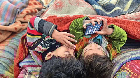 Homeless children play with a mobile phone at a night shelter on a chilly day
