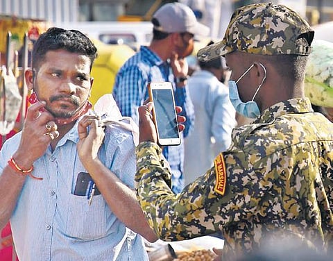 A BBMP marshal takes photos of a man not wearing a mask, to impose a fine, at KR Market in Bengaluru on Tuesday | SHRIRAM BN