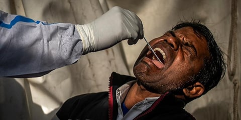 A man reacts as a health worker collects his swab sample to test for COVID-19 at a train station in New Delhi. (Photo | AP)