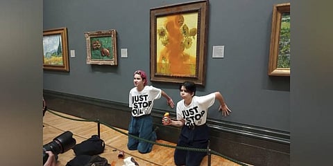 Handout photo issued by Just Stop Oil of two protesters who have thrown tinned soup at Vincent Van Gogh's famous 1888 work Sunflowers at the National Gallery in London. (Photo | AP)