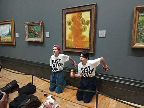 Handout photo by Just Stop Oil of two protesters who have thrown tinned soup at Vincent Van Gogh's famous 1888 work Sunflowers at the National Gallery in London, Friday Oct. 14, 2022. (AP)