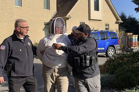 Rorie S. Woods, 55, center, wears a beekeeping suit while taken into custody by Hampden County Sheriff's Department officers, in Longmeadow, Mass., Wednesday, Oct. 12, 2022. (Photo | AP)