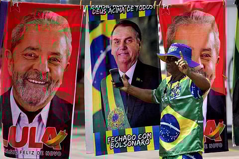 A demonstrator dressed in the colors of the Brazilian flag performs in front of a street vendor's towels for sale featuring Brazilian presidential candidates in Brasilia. (File Photo | AP)