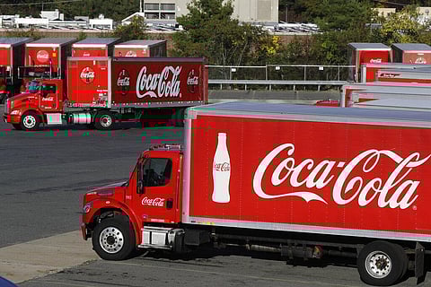 A truck with the Coca-Cola logo, behind left, maneuvers in a parking lot at a bottling plant. (File photo | AP)