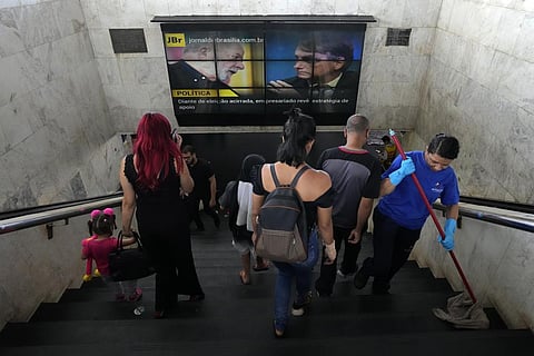 Commuters at a bus station walk below a screen showing Brazil's former President Luiz Inacio Lula da Silva, left, and current President Jair Bolsonaro in Brasilia, Monday, Oct. 3, 2022. (Photo | AP)