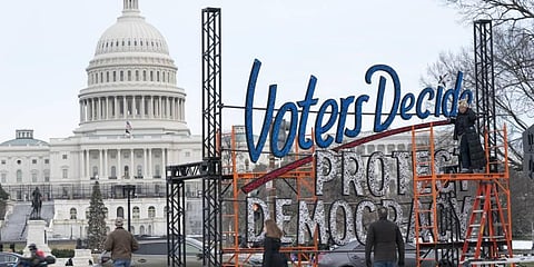 With the U.S. Capitol in the background, people walk past a sign that says say, 'Voters Decide Protect DemocracY. (Photo | AP)