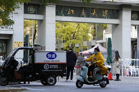 A woman wearing mask rides past an entrance to Peking University in Beijing, Wednesday, Nov. 16, 2022. (Photo | AP)