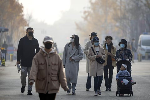 People wearing face masks walk along a pedestrian shopping street at the Wangfujing shopping district in Beijing (Photo | AP)