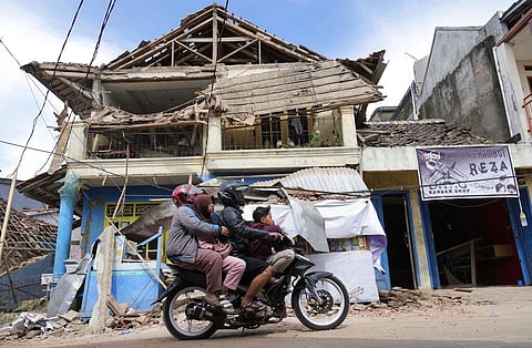 People ride a motorbike past a building damaged in Monday's earthquake in Cianjur, West Java, Indonesia. (Photo | AP)