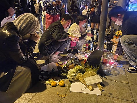 Residents mourn for the victims of a recent deadly fire at a residential building in Urumqi city at a road sign of the Middle Wulumuqi Road or Middle Urumqi Rd in Shanghai, China. (Photo | AP)