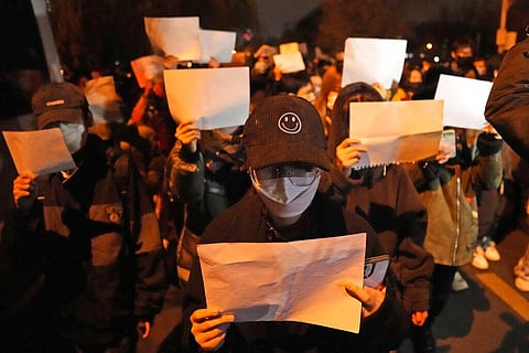 Protesters hold up blank papers and chant slogans as they march in protest in Beijing, Sunday, Nov. 27, 2022. (Photo | AP)