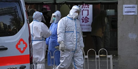 An ambulance worker in protective gear walks by medical workers chat each others as residents wait to enter the fever clinic of a hospital in Beijing, Tuesday, Dec. 13, 2022.(Photo | AP)
