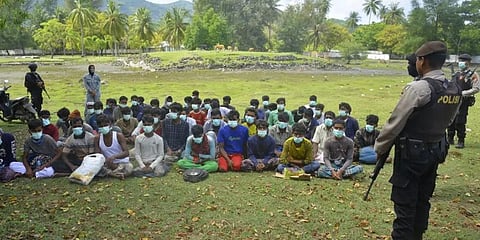 A policeman (top) stands guard next to a group of Rohingya refugees waiting to be transferred to a temporary shelter. (Photo | AFP)