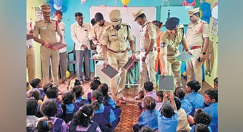Police personnel distribute slates to the students of Dhruva school in Gourdeddipet village near Peddapalli