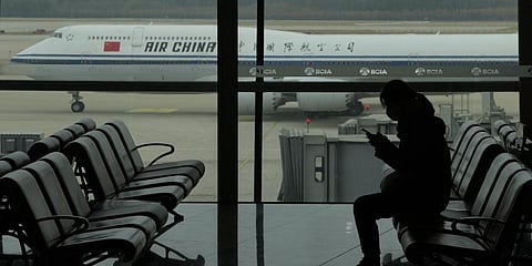 A passenger checks her phone as an Air China passenger jet taxi past at the Beijing Capital International airport in Beijing.(File Photo | AP)
