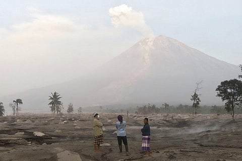 Villagers stand on an area covered in volcanic ash as Mount Semeru looms in the background in Kajar Kuning village in Lumajang, East Java, Indonesia | AP