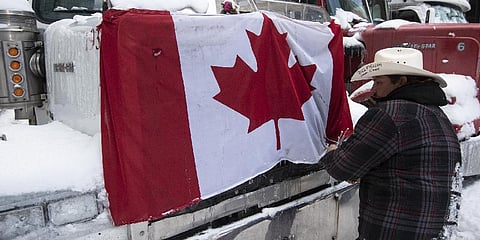 A trucker removes a flag of Canada from the hood of their vehicle as truckers prepare to drive away after police intervention.(Photo | AP)