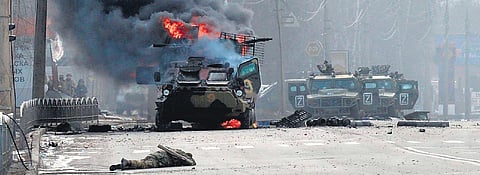 A Russian armoured personnel carrier burning near the body of an unidentified soldier in Ukraine’s Kharkiv on Sunday. (Photo | AFP)