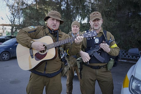 Members of the Ukrainian civil defense, one mimicking a guitar with his assault rifle, play a song while waiting to escort a fuel transport in Kyiv, Ukraine. (Photo | AP)
