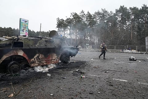 A volunteer of Ukraine's Territorial Defense Forces walks by a damaged armored vehicle at a checkpoint in Brovary, outside Kyiv,. ( Photo | AP)