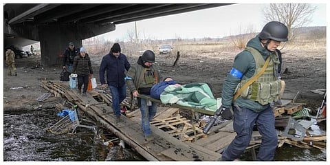 Ukrainians soldiers pass an improvised path under a destroyed bridge as they evacuate an elderly resident in Irpin, northwest of Kyiv on Saturday. (Photo | AP)