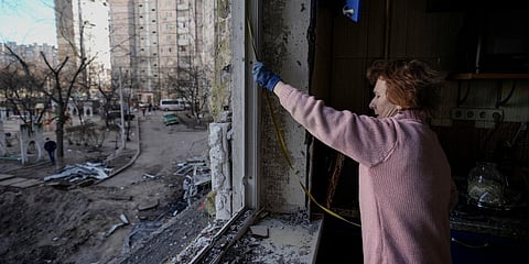 A woman measures a window before covering it with plastic sheets in a building damaged by a bombing the previous day in Kyiv. (Photo| AP)