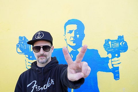 Street artist Todd Goodman, known as 1GoodHombre, stands in front of his stencil of Ukrainian President Volodymyr Zelenskyy holding submachine guns. (Photo | AP)