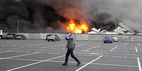 A person walks past as fire and smoke rises over a damaged logistic center after shelling in Kyiv, Ukraine. (Photo | AP)